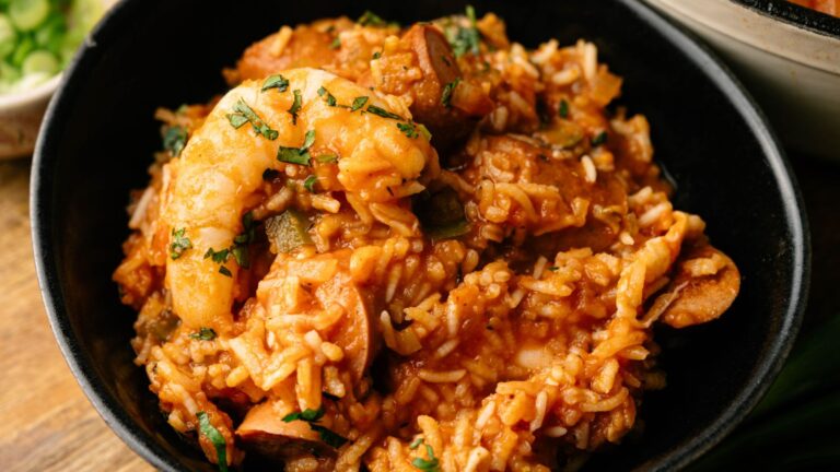 A bowl of jambalaya with shrimp, sausage, vegetables, and rice, garnished with chopped herbs.