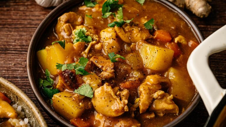 A bowl of chicken stew with potatoes, carrots, and fresh herbs, served on a wooden table.
