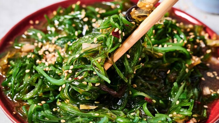 A plate of seaweed salad topped with sesame seeds, with chopsticks lifting a portion.