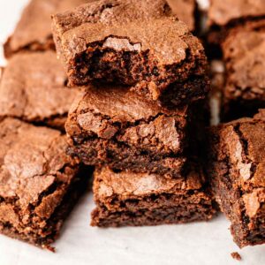 A stack of delicious protein brownies sits on parchment paper, with one brownie at the top showing a tempting bite taken out of it.