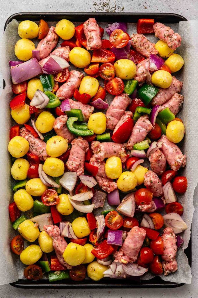 Sheet Pan Gnocchi with sausage pieces, cherry tomatoes, red onion, and bell peppers arranged on parchment paper—ready for a simple and flavorful one-pan meal.