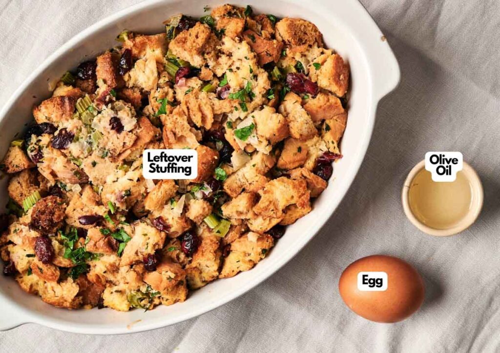 Oval casserole dish filled with leftover stuffing, perfect for making Air Fryer Stuffing Balls, sits next to a small bowl of olive oil and a whole egg on a white surface. Labels identify each item.