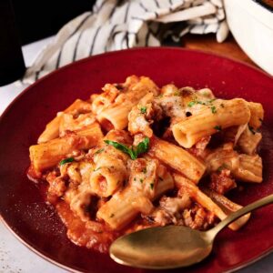 A plate of Air Fryer Baked Ziti with tomato sauce, ground meat, melted cheese, and fresh herbs, served with a gold-colored spoon.