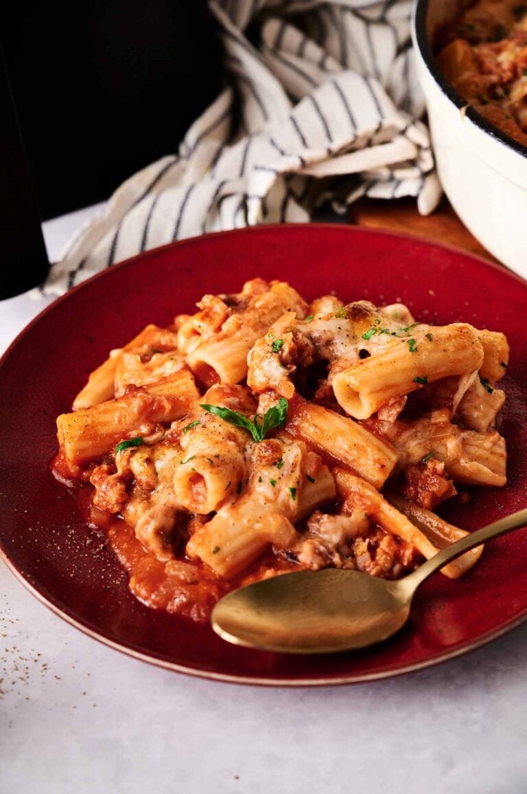 A plate of Air Fryer Baked Ziti with tomato sauce, ground meat, melted cheese, and fresh herbs, served with a gold-colored spoon.