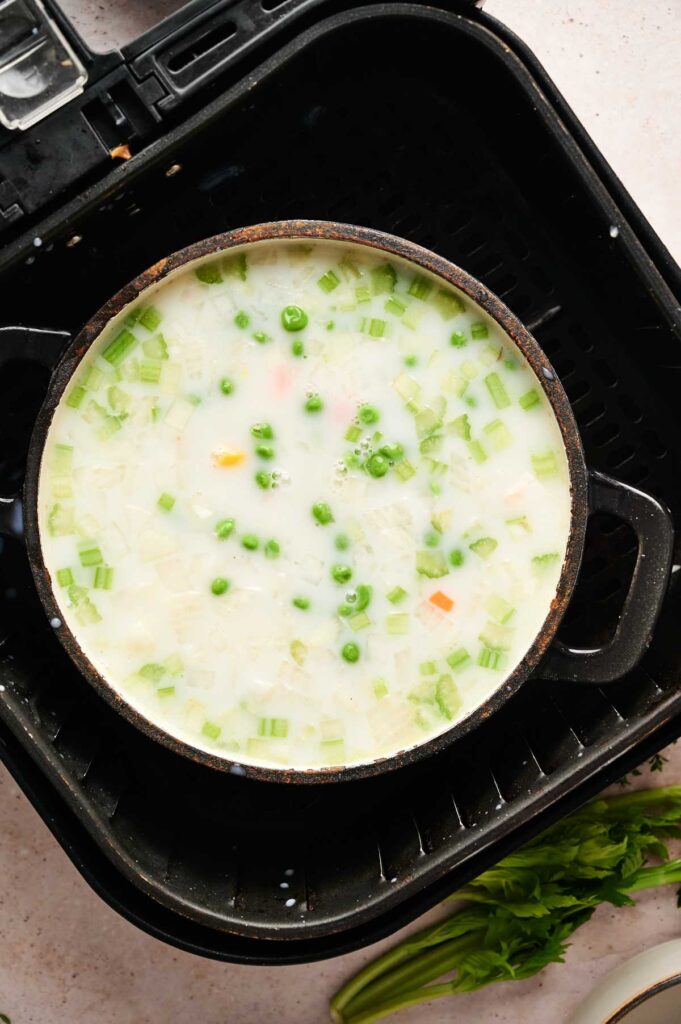 A pot of creamy Air Fryer Chicken Pot Pie Soup with peas, celery, and diced vegetables sits inside an air fryer basket.