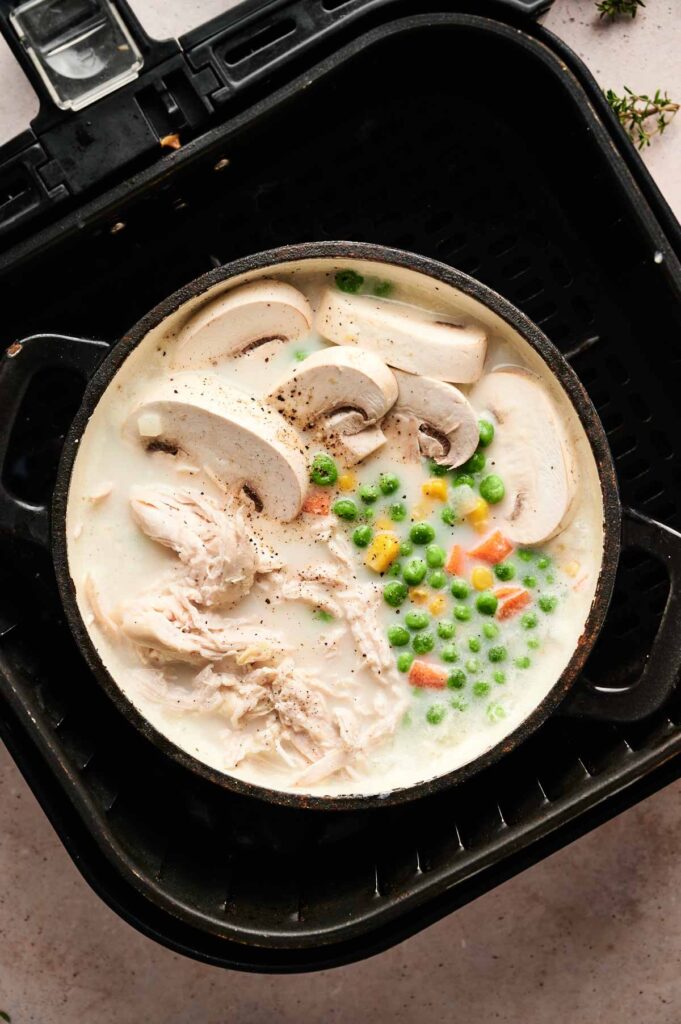 A black pan filled with creamy Air Fryer Chicken Pot Pie Soup—brimming with shredded chicken, sliced mushrooms, peas, and carrots—sits temptingly inside an air fryer basket.