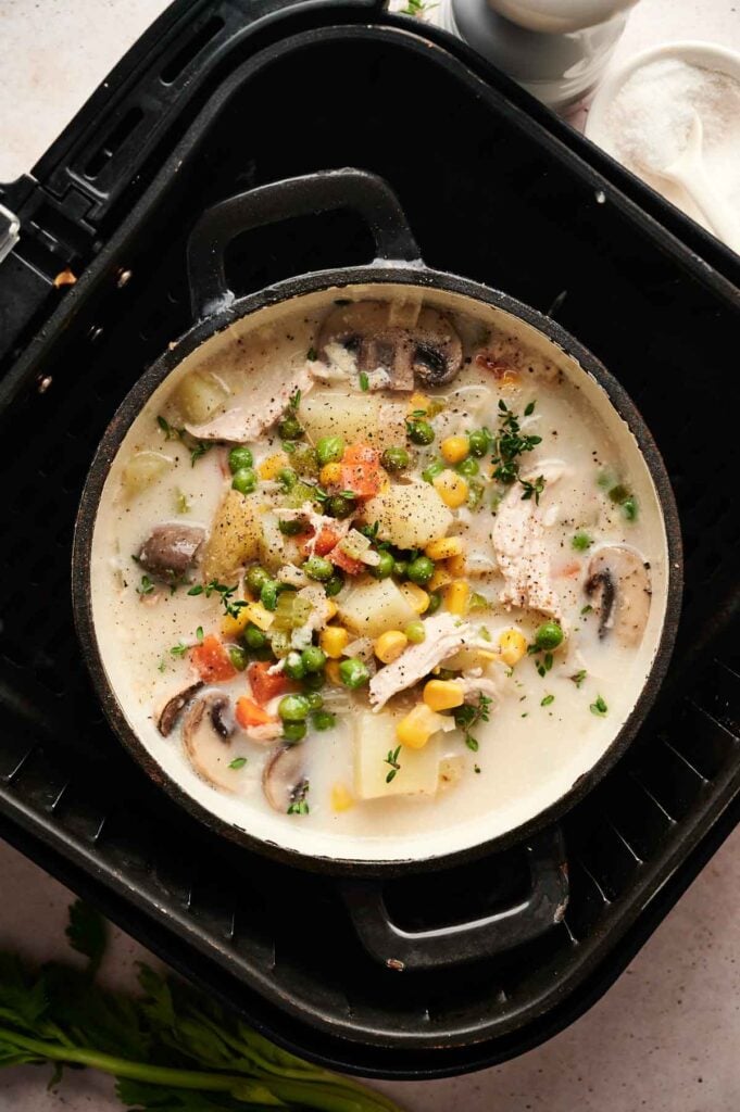 A pot of creamy Air Fryer Chicken Pot Pie Soup with potatoes, peas, corn, mushrooms, and carrots sits warm inside an air fryer tray.