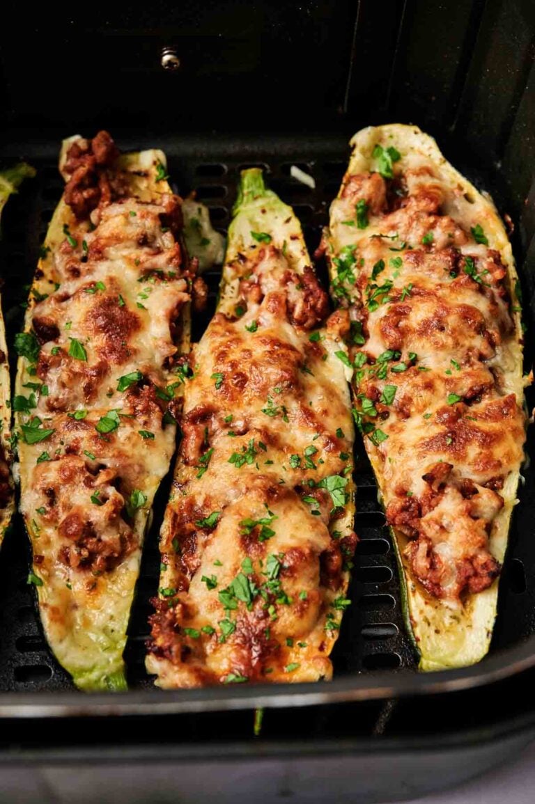 Three Air Fryer Zucchini Boats filled with ground meat and melted cheese, garnished with chopped herbs, inside an air fryer basket.