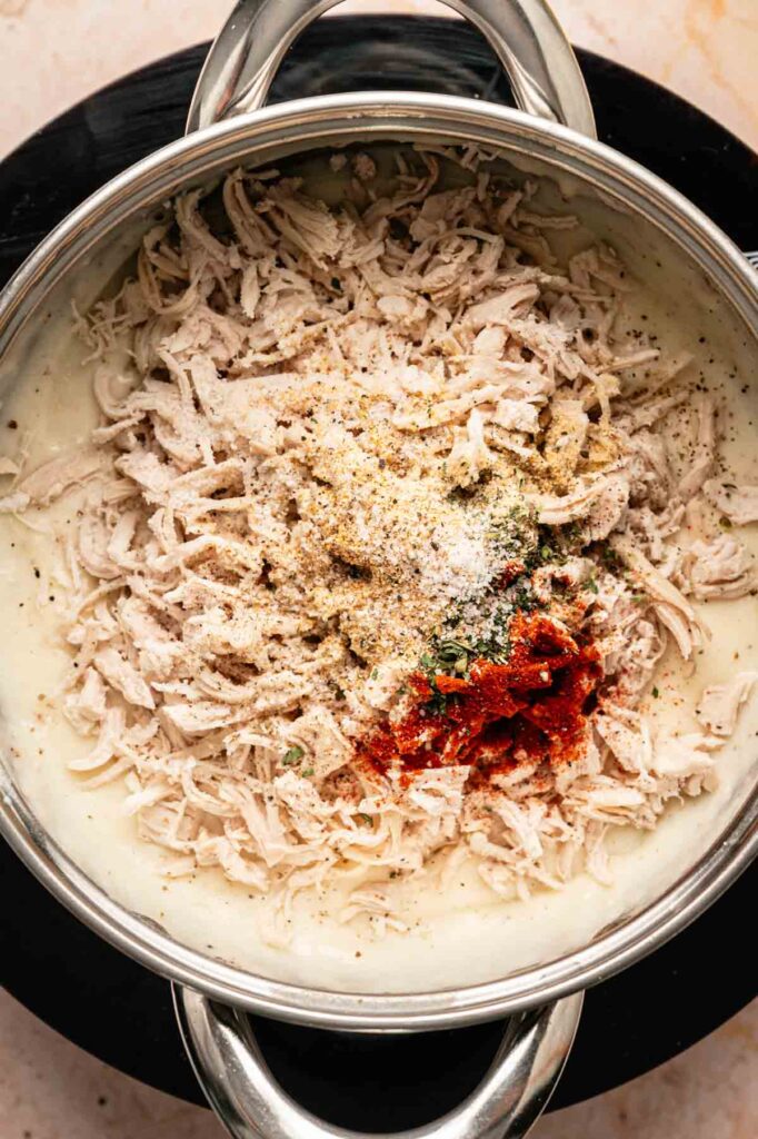 A pot filled with shredded chicken, creamy white sauce, and a mix of spices including paprika and herbs—ingredients that come together perfectly for making delicious Chicken Croquettes—seen from above.