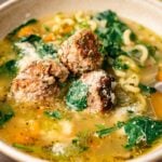 A bowl of Italian Wedding Soup with meatballs, spinach, pasta, carrots, and savory broth, topped with grated cheese.