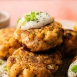 Salmon Patties topped with sour cream and sliced green onions, garnished with fresh herbs, and beautifully served on a plate.