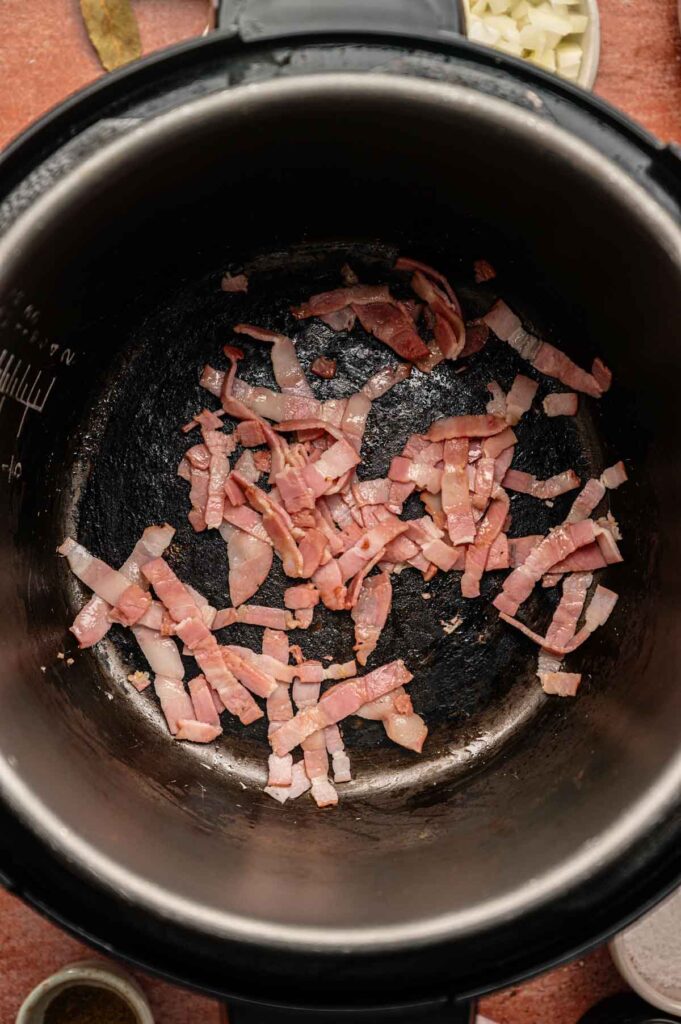Thin slices of bacon sizzling in the bottom of a black pot, with some chopped onions and spices visible in small bowls nearby—perfect ingredients for starting a classic Hoppin’ John recipe.