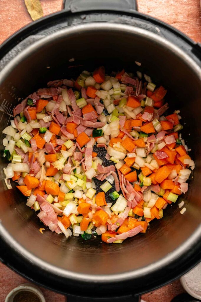 Chopped bacon, carrots, celery, and onion in a metal pot, ready to be cooked for a flavorful Hoppin’ John dish.