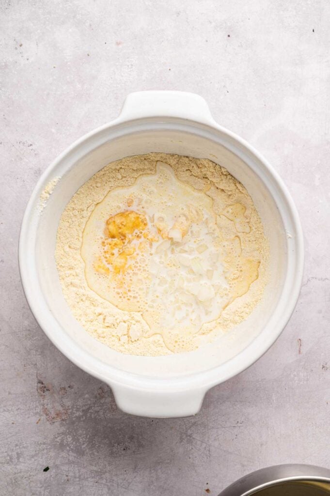 Egg and milk mixture with diced onion sitting in a well of dry hush puppy ingredients