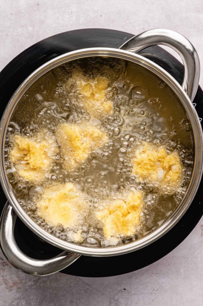 Hush puppy batter frying and bubbling in a pot of hot oil