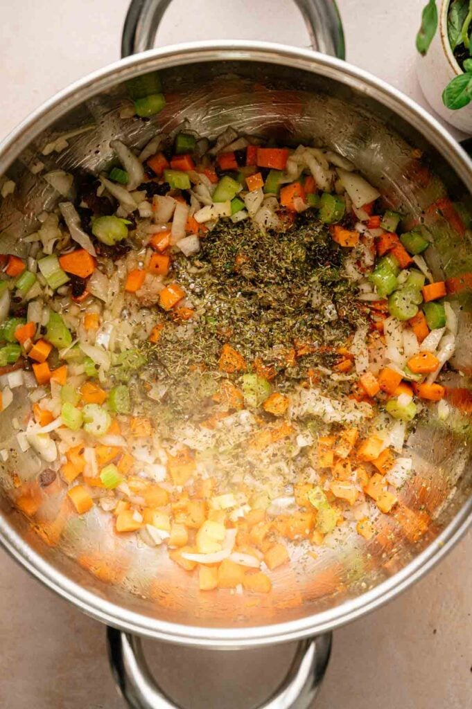 Chopped onions, carrots, and celery with dried herbs are sautéing in a stainless steel pot—the perfect aromatic base for classic Italian Wedding Soup.