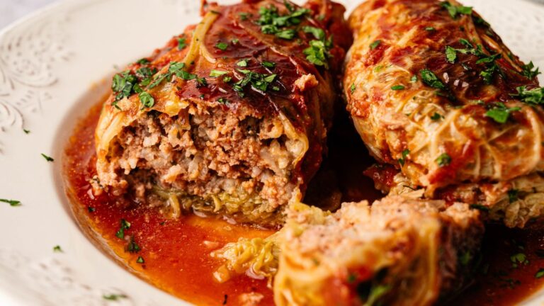 Two cabbage rolls stuffed with ground meat and rice, topped with tomato sauce and chopped herbs, served on a white plate.