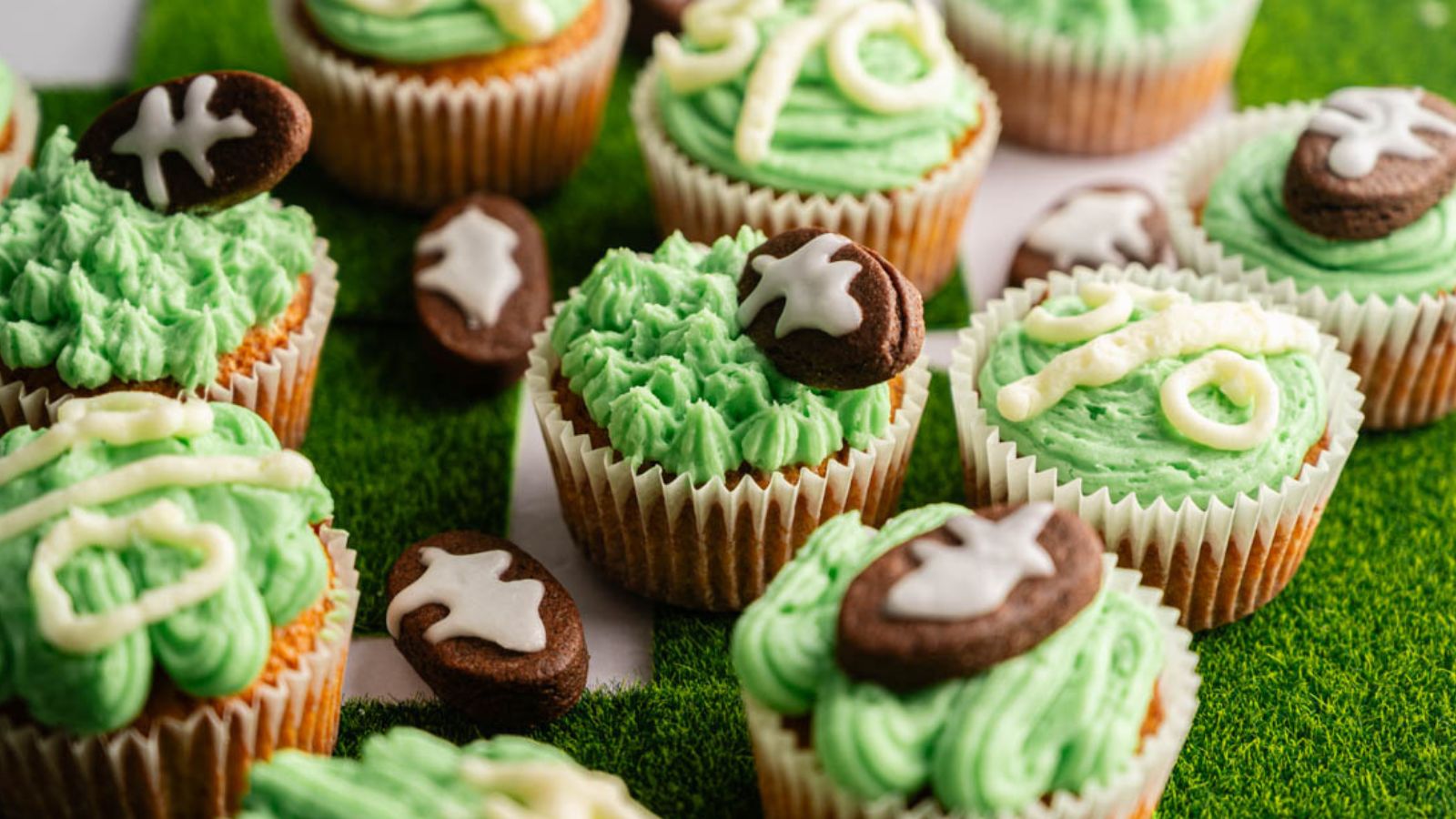 Cupcakes decorated with green frosting and chocolate footballs, arranged on a surface resembling a grass field.