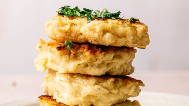 A stack of three golden-brown fritters garnished with chopped herbs on a white plate.