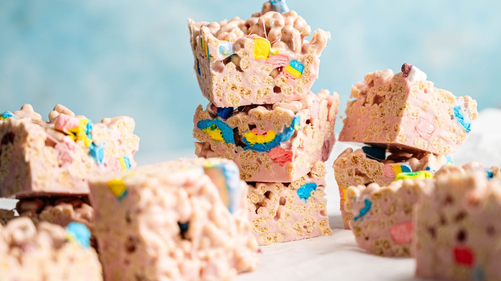 A close-up of stacked cereal treats made with colorful marshmallows and crispy cereal pieces, set against a light blue background.