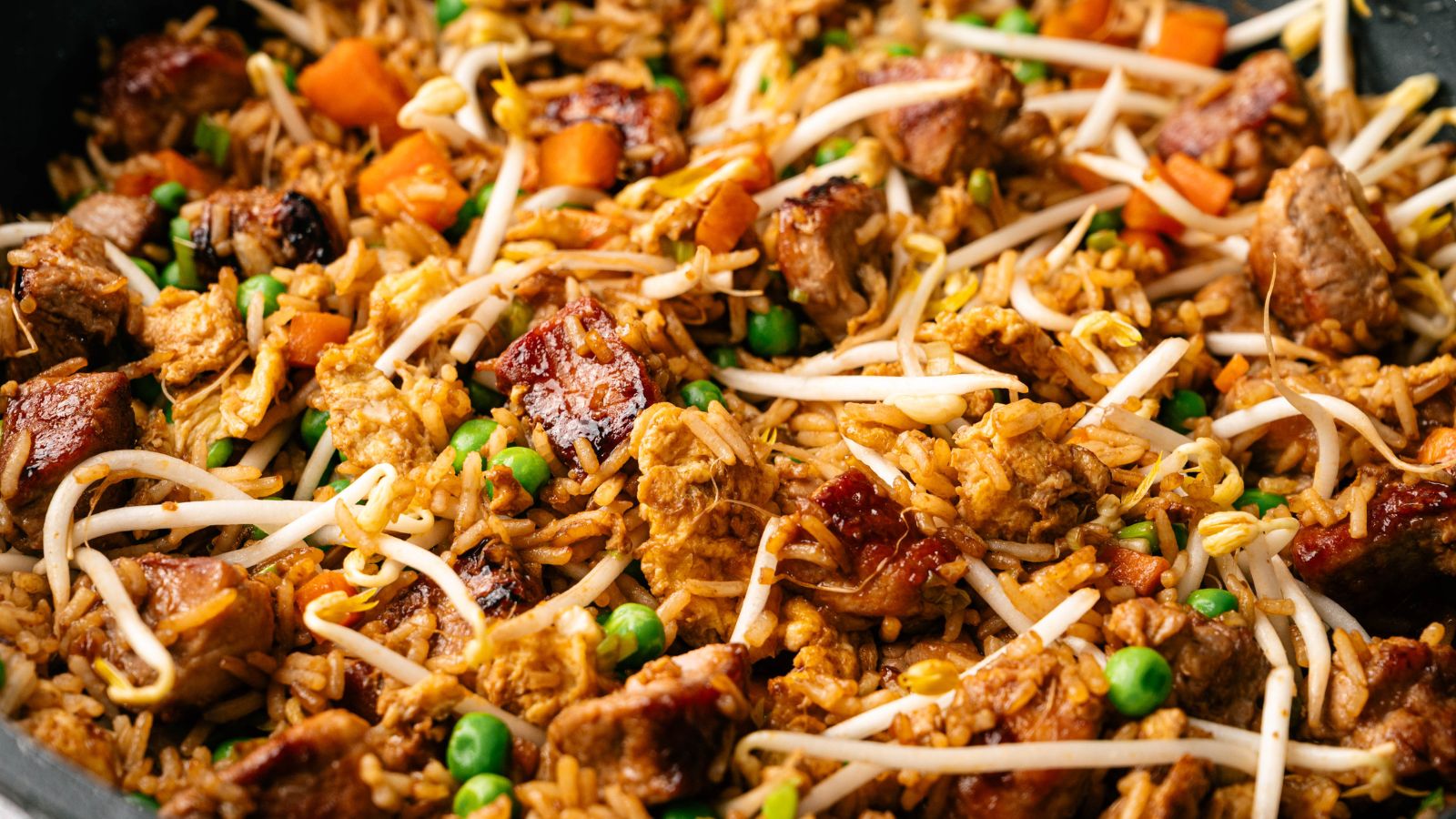 Close-up of fried rice with chunks of meat, peas, diced carrots, and bean sprouts mixed together.