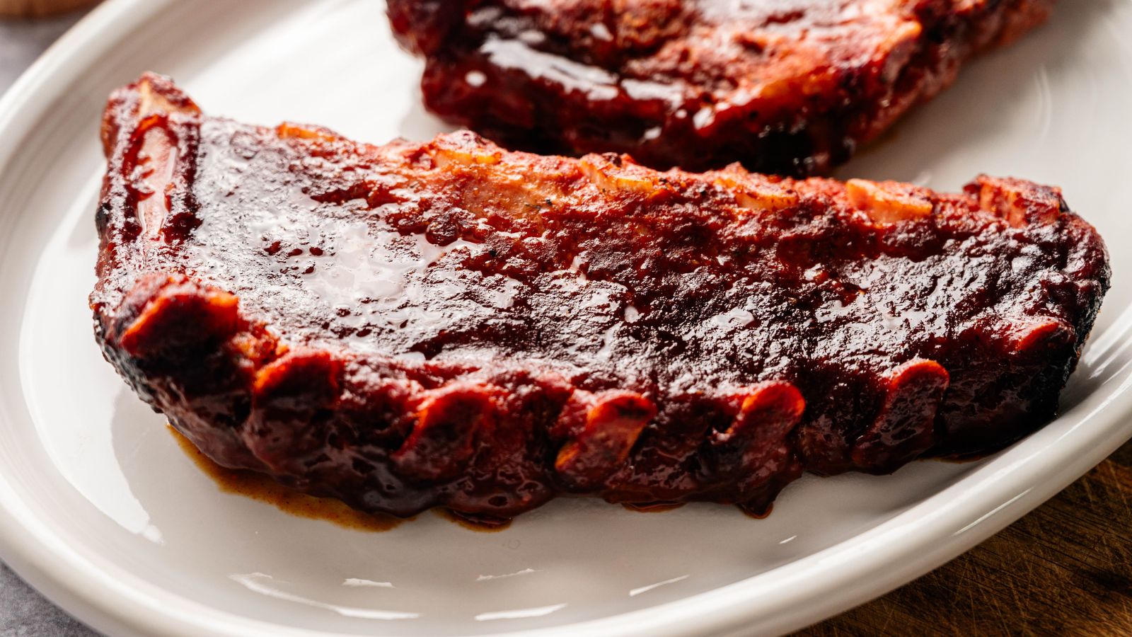 A close-up of a barbecued pork rib with a glossy layer of barbecue sauce on a white plate.