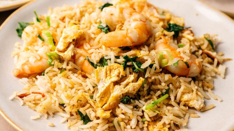 A plate of shrimp fried rice with pieces of egg, green onions, and leafy greens.