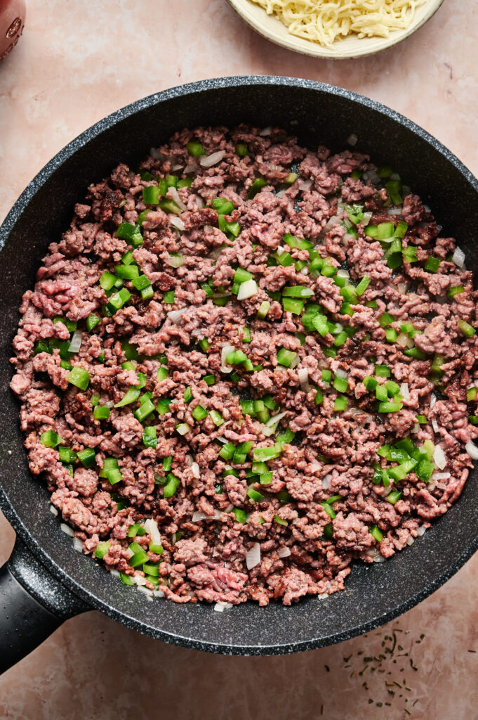 Ground beef and chopped green peppers cooking in a black skillet on a light-colored countertop—a delicious start for your next Air Fryer Pizza Casserole.