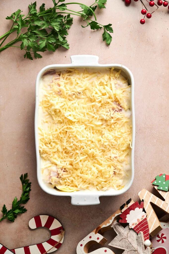 A rectangular baking dish filled with creamy Air Fryer Scalloped Potatoes and Ham, topped with shredded cheese, surrounded by parsley and festive holiday decorations.