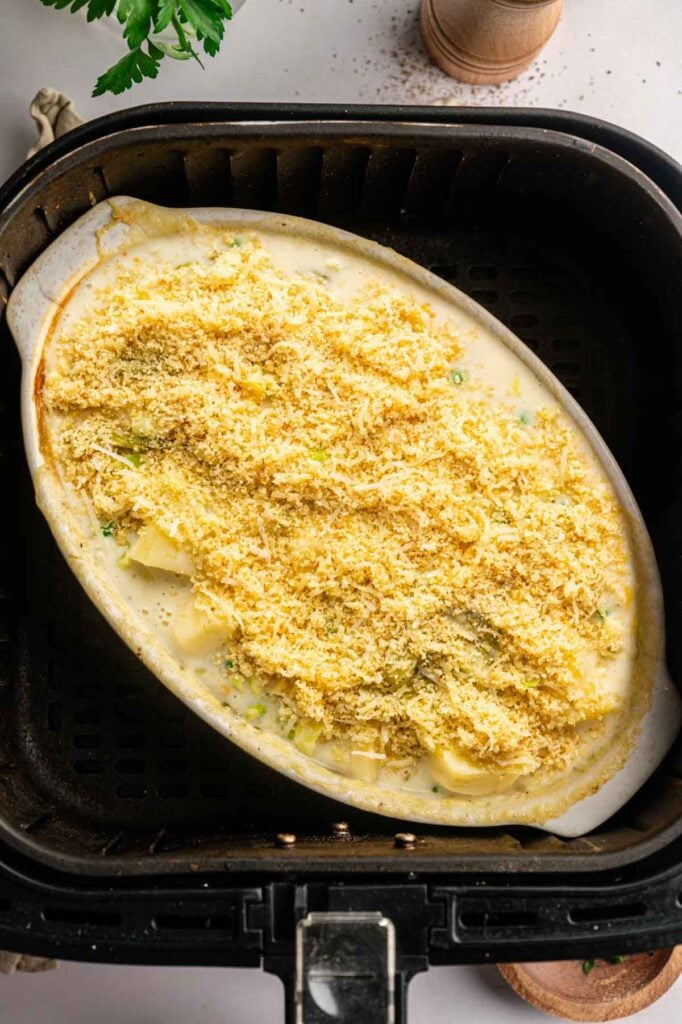 An oval casserole dish filled with a creamy, shredded cheese-topped mixture sits inside an air fryer basket, ready to become the perfect Air Fryer Easter Casserole.