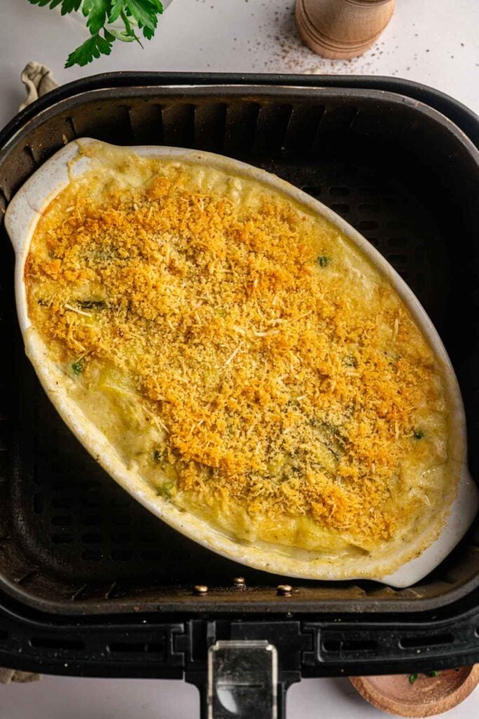 Oval dish with a cheesy, golden-brown breadcrumb topping on a baked Air Fryer Easter Casserole, sitting inside an air fryer basket.