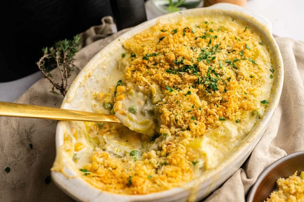 Oval casserole dish of creamy Air Fryer Easter Casserole, topped with golden breadcrumbs and partially served with a spoon.