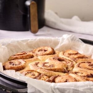 A tray lined with parchment paper holds freshly baked Air Fryer Orange Rolls; an air fryer is visible in the background.