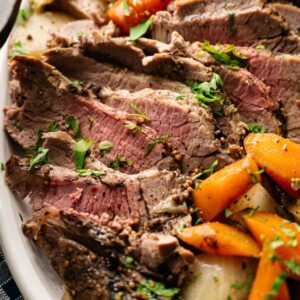 Sliced roast beef served on a plate with cooked carrots and potatoes, reminiscent of a classic Corned Beef and Cabbage meal, garnished with chopped parsley.
