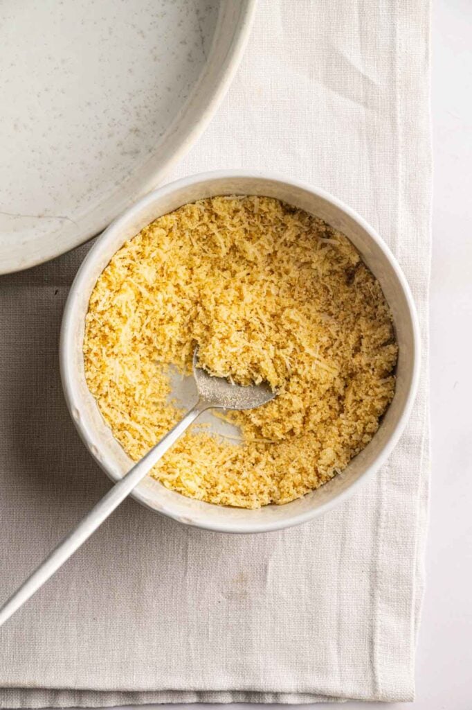 A bowl filled with yellow, crumbly mixture and a spoon on a light cloth napkin, with part of another bowl—perhaps holding more of the Air Fryer Easter Casserole—visible nearby.