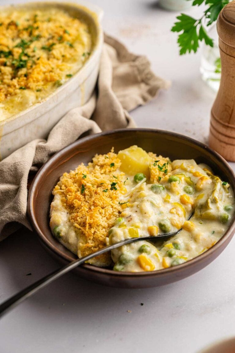 A bowl of creamy Easter Casserole topped with golden breadcrumbs sits next to a baking dish filled with the same comforting casserole.