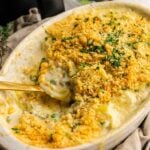 Oval dish of creamy Air Fryer Easter Casserole topped with golden breadcrumbs and chopped herbs, with a serving spoon in the dish and some casserole scooped out.