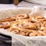 A baking pan lined with parchment paper holds freshly baked Air Fryer Orange Rolls arranged closely together.