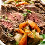 Slices of medium-rare roast beef arranged on a plate with cooked carrots, potatoes, fresh herbs, and a nod to Corned Beef and Cabbage for a classic touch.