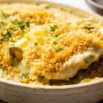 A close-up of a creamy Easter Casserole topped with golden breadcrumbs being served from a round baking dish.