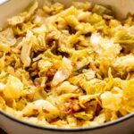 Fried Cabbage chopped and cooked in a white pot, lightly browned and mixed with small pieces of onion and seasoning.