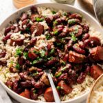 A bowl of Red Beans and Rice featuring sliced sausage, topped with chopped parsley, with a fork resting in the dish.