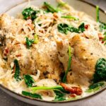 A bowl of creamy Slow Cooker Chicken Thighs with wilted spinach, sliced onions, sun-dried tomatoes, and a peppered cream sauce.