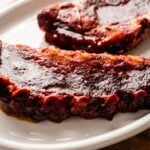 Two pieces of slow cooker ribs covered in sauce are served on a white oval plate.