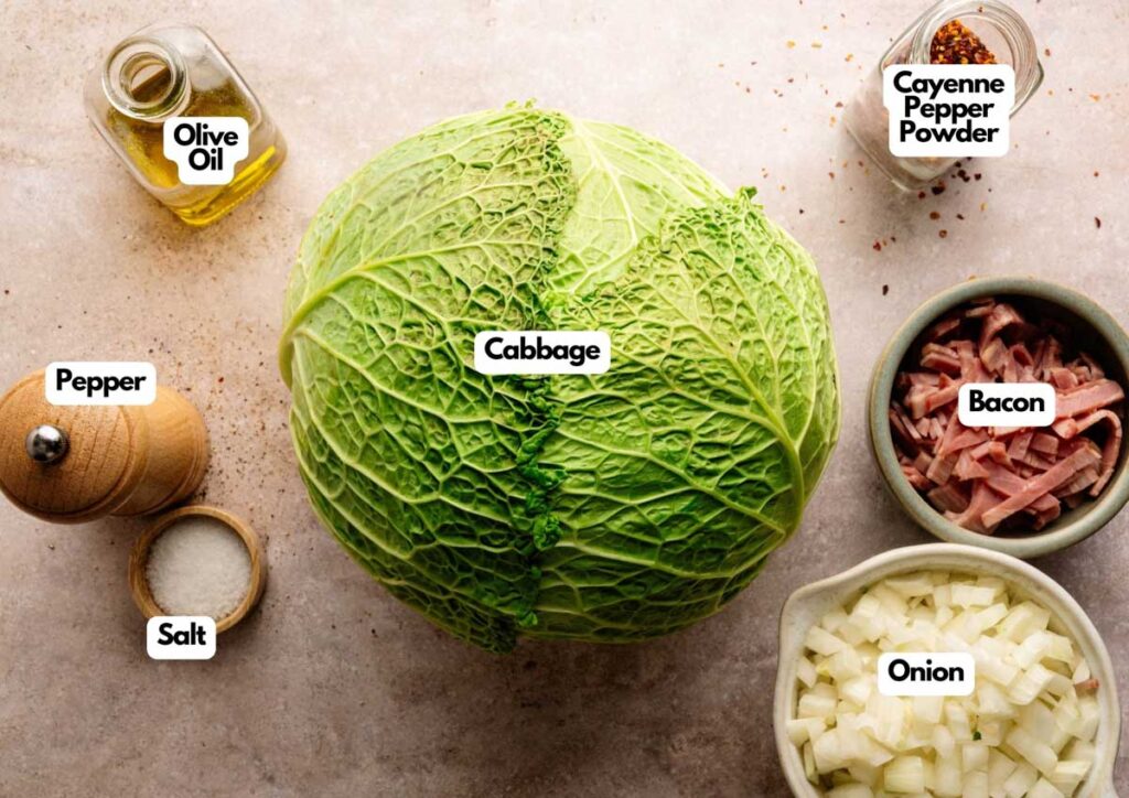 A head of cabbage surrounded by bowls of chopped onion, bacon, salt, pepper, cayenne pepper powder, and a bottle of olive oil—all labeled and ready for making delicious Fried Cabbage.