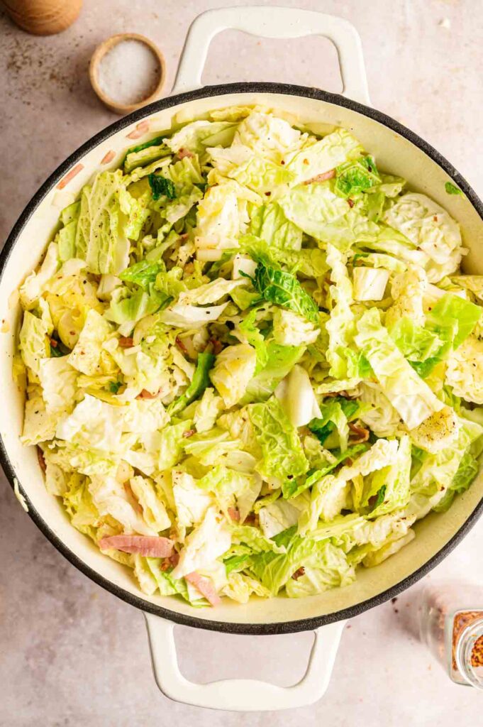 Chopped lettuce salad with sliced ham and dressing in a white ceramic bowl, viewed from above on a light surface—perfect alongside a serving of savory fried cabbage.