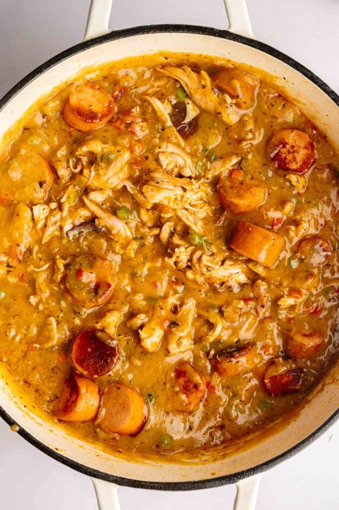 A pot of thick gumbo stew with shredded chicken, sausage slices, and vegetables in a brown, seasoned broth.
