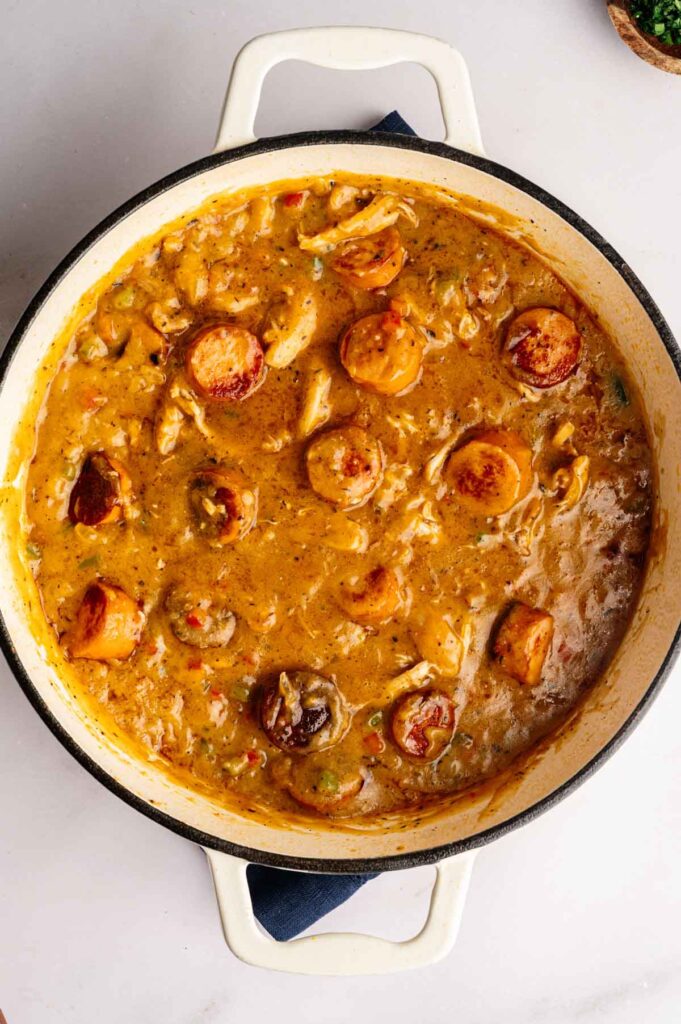 A pot filled with thick, creamy gumbo featuring tender chicken, savory sausage slices, and fresh vegetables simmered in a rich brownish sauce.