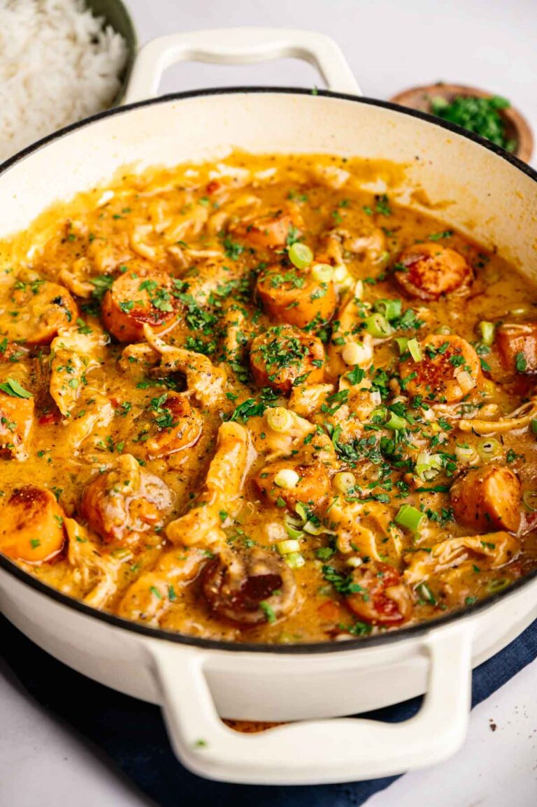 A white pot filled with savory gumbo, brimming with sausage, chicken, and vegetables, garnished with chopped green onions and parsley.
