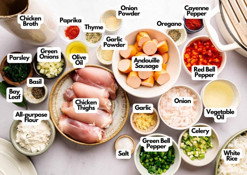 An assortment of labeled gumbo ingredients for a recipe, including chicken thighs, andouille sausage, spices, chopped vegetables, broth, flour, rice, and oils, all arranged on a countertop.